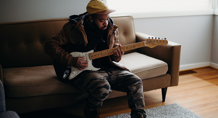 Musician Sitting on a Couch Playing Guitar - Toggle Insurance