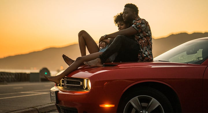 Man and woman sitting on the hood of a car in the sunset