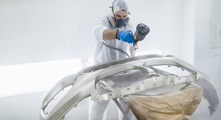 man painting a car white in an auto body shop