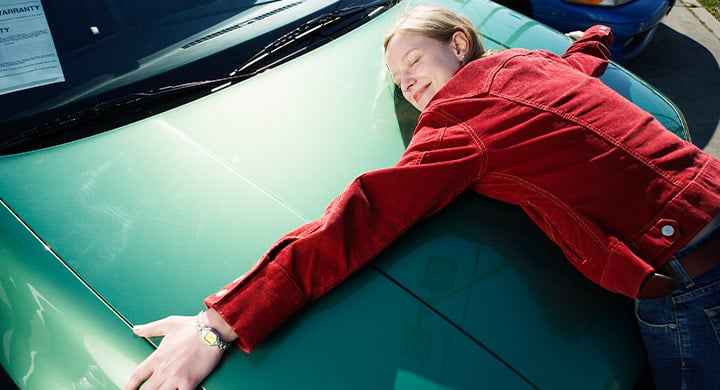 woman in a red jacket hugging a green car