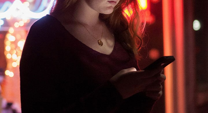 woman using smartphone in front of red and blue lighted glass store