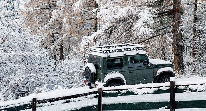 A jeep is parked in the snow near a fence