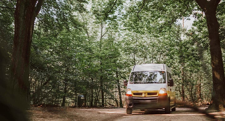 a van is driving down a wooded road