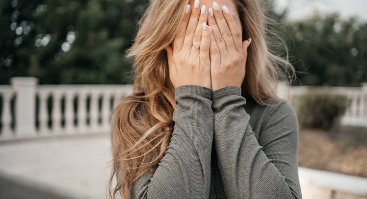 Woman with long hair and a grey sweater covering her face with her hands