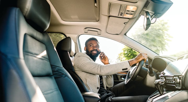 Young African American man in smart casual business wear, using phone sitting in the car, side view.